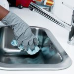 Femme qui nettoie un évier en inox avec un chiffon et des gants